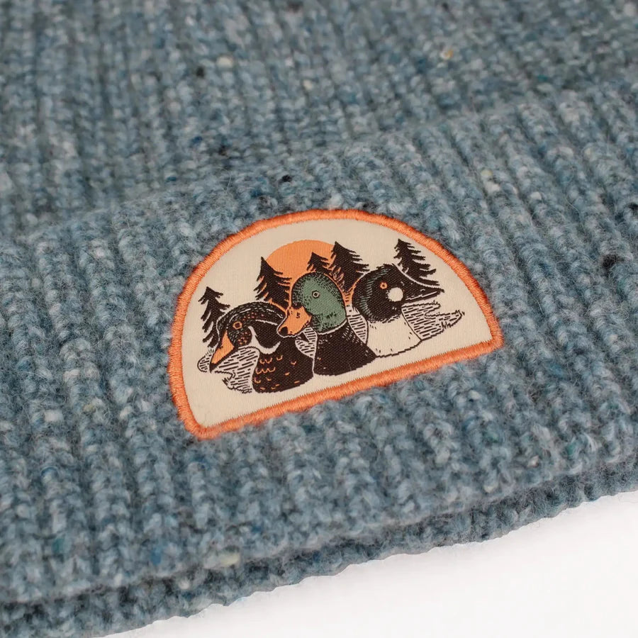 Duck Trio Wool Blend Beanie, Lake: Close-up of a teal-blue knit beanie with a woodland patch of three ducks, perfect for warmth and showcasing birdwatching passion.