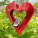 Fly Thru Red Heart Copper Bird Feeder with a grey songbird perched on it, showcasing its open-top heart shape and durable red copper finish.