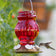 Ruby Visions Antique Glass Gravity Hummingbird Feeder with red textured glass, white flower-shaped ports, and a hummingbird feeding.