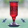 Red Jewel Hummingbird Feeder with embossed decorative hummingbirds, red flower-shaped feeding ports, metal hanger, and wraparound perch, attracting two flying hummingbirds.