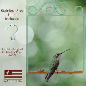 A stainless steel hummingbird feeder swing hook shown on a light green bokeh background, with a hummingbird perched on the feeder. Text on the left reads 'Stainless Steel Hook Included' and 'Specially designed for hanging Pop's Swings,' with a 'Made in USA' flag graphic at the bottom.